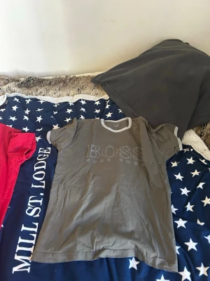 Grå BOSS t-shirt med kontrastkrage - Snygg grå t-shirt från Hugo Boss med ljusgrå kontrastkrage och ärmslut. Stort BOSS-tryck framtill. Tillverkad i mjuk bomull med lite lycra för extra stretch. Perfekt för en avslappnad och stilren look.