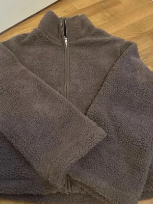 Beige teddyjacka med dragkedja stl M - Mysig  teddyjacka i fluffigt material med hög krage och hel dragkedja framtill. Jackan har lång ärm och en avslappnad passform, perfekt för kyliga dagar. Materialet är mjukt och ger en skön känsla. Enkel och stilren design utan synliga loggor.