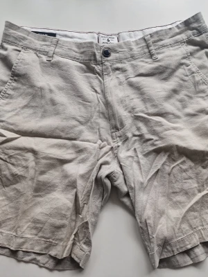 Beige shorts från Jack & Jones - Snygga beige shorts från Jack & Jones med klassisk passform. De har fickor fram och bak, bälteshällor och stängs med knapp och dragkedja. Perfekta för varma dagar och enkla att matcha med olika outfits.