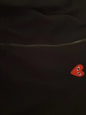 Svart hoodie Comme des Garçons Play - Svart hoodie med dragkedja från Comme des Garçons Play. Klassisk design med det ikoniska röda hjärtat med ögon på bröstet. Mjuk bomullskvalitet och huva med snörning. Perfekt för en stilren och trendig look.