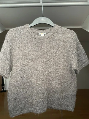 Stickad t-shirt - Mysig grå/brun stickad t-shirt med korta ärmar och rund hals. Tröjan har en fluffig och mjuk textur och skulle säga att den är i strl XS/S