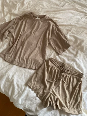 Beige ribbad loungewear-set - Mysigt loungewear-set i beige med ribbad struktur. Setet består av en oversized t-shirt med rund hals och korta ärmar samt matchande shorts med dragsko och elastisk midja. Perfekt för chill dagar hemma.