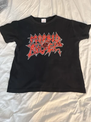 Svart Morbid Angel t-shirt - Cool svart t-shirt med Morbid Angel-logga i rött och vitt framtill. Trycket har en tydlig metalstil med pentagram och taggiga bokstäver. Perfekt för dig som gillar bandmerch och vill sticka ut med en edgy look. Magtröja, storlek S/M