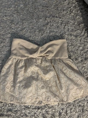 Beige tubtopp med broderade blommor SHEIN - Söt beige tubtopp från SHEIN med broderade blommor och hålmönster. Toppen har en twistad detalj framtill och är tillverkad i ett lätt material som passar perfekt till varma dagar.