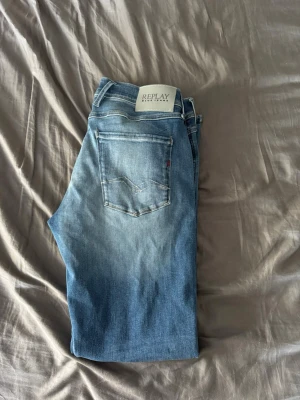 Blå jeans från Replay - Säljer ett par klassiska blå jeans från Replay med fem fickor och diskret logga på bakfickan. Och är tillverkade i mjukt denimtyg. Perfekta för en avslappnad stil. Modellen är anbass och har en slim fit passform dem har dessutom hyperflex för comfort. Är helt oanvända.
