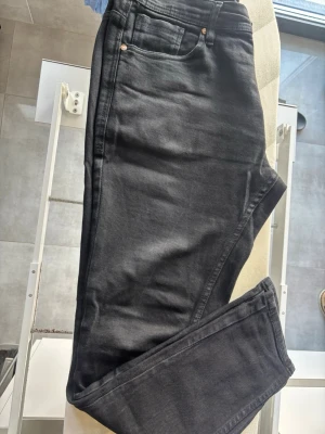 Svarta jeans från Zara - Säljer ett par svarta jeans från Zara med klassisk femficksmodell och knappgylf. Jeansen har en normal passform och är tillverkade i bomull med lite stretch för extra komfort. Perfekta till alla typer av outfits.