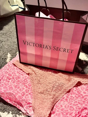 Spetsstring i rosa från Victoria's Secret - Säljer ett par snygga stringtrosor i ljusrosa spets från Victoria's Secret. Trosorna har en feminin design med bred spetskant och genombrutet mönster som ger en romantisk känsla. Perfekta för dig som gillar både stil och komfort.