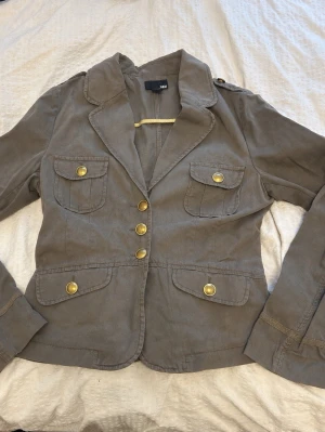 Beige kavajjacka från H&M med guldknappar - Stilren beige kavajjacka från H&M med fyra fickor framtill och snygga guldknappar. Storlek 40, jag är storlek 36 för referens.