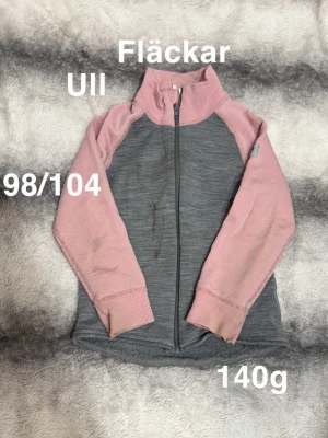 Grå och rosa ullziptröja med hög krage - En snygg ullziptröja i grått med rosa ärmar och hög krage. Tröjan har raglanärm, ribbade muddar och dragkedja framtill. Perfekt för lager-på-lager och chill dagar.🌸Obehandlade fläckar. Ull. Tvättad med ulltvättmedel. Storlek 98/104 