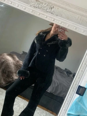 Svart kappa med fuskpälsdetaljer - EJ RIKTIG PÄLS. Jättefint skick, sparsamt använd, inga fläckar, inget tecken på slitage och inga sömmar uppe. Denna går inte att köpa varken online/butik längre. Nypris ca 1199kr  Säljes pga ej kommer till användning.