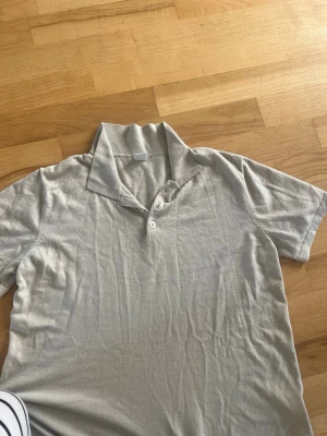 Beige piké med krage och knappar Lindex - Stilren beige pikétröja med klassisk krage och två knappar framtill. Kortärmad modell i mjukt material, perfekt för en avslappnad och snygg look.
