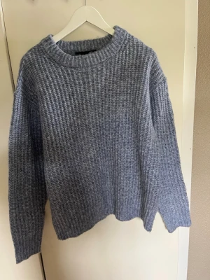Grå stickad oversized tröja - Mysig grå stickad tröja med grov ribbad struktur och rund hals. Tröjan har en oversized passform och långa ärmar, perfekt för kyliga dagar. Enkel och stilren design som passar till det mesta.
