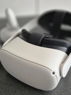 VR Quest 2 med Elite Strap och laddningsstation - Säljer ett Oculus Quest 2 VR-headset i vit plast med svarta detaljer. Inkluderar två vita handkontroller, laddstation, extra batterier och lila silikonöverdrag. Perfekt för gaming och VR-upplevelser hemma. Obs ! Kontrollera och vr har skrapor men funkar bra!  Repet till Kontrollera är borta fast har lilla handkontroll !