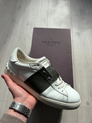 Open Sneaker - Vita sneakers från Valentino med mörkgrön detalj. Skorna är i genrellt fräscht skick men tecken på användning finns, dessvärre inga hål eller något som påverkar användning. Storlek 43, men då denna modell anses som något stora i storleken kan även 43,5/44 fungera, fråga om innermått vid intresse. Skorna säljes med låda, kuvert med kort samt en dustbag. 