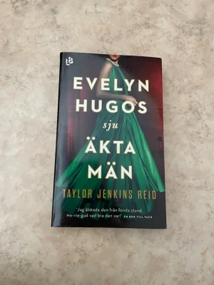 Evelyn Hugos sju äkta män - En roman med svart omslag och bild på en kvinna i en grön klänning. Titeln 'Evelyn Hugos sju äkta män' är tryckt i stora guldfärgade bokstäver. Författare: Taylor Jenkins Reid. Boken är på svenska och har ett elegant, modernt utseende.