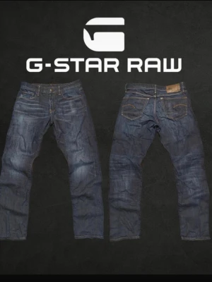 Mörkblå jeans från G-Star Raw - Snygga mörkblå jeans från G-Star Raw med klassisk femficksmodell och raka ben. Jeansen har slitningar och tvättade detaljer för en cool, avslappnad look. Tillverkade i robust denim med logopatch bak i midjan.