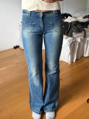 Blå bootcut jeans med fickdetaljer - Snygga blå bootcut jeans med ljusa slitningar och unika fickdetaljer framtill. Jeansen har normal midja, klassisk dragkedja och knapp. Perfekta för dig som gillar en avslappnad men trendig look.