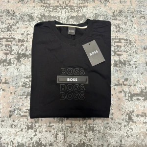 Svart t-shirt med tryck - Snygg svart t-shirt med stilrent tryck av loggan i flera lager på bröstet. Klassisk rund hals och korta ärmar. Perfekt för dig som gillar enkel men trendig design. Tillverkad i mjuk bomull för skön känsla hela dagen.