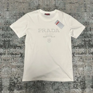 Vit t-shirt  - Snygg vit t-shirt med diskret logga och emblem på bröstet. Klassisk passform och rund halsringning. Perfekt för dig som gillar stilrena och exklusiva plagg. Tillverkad i mjuk bomull för maximal komfort.