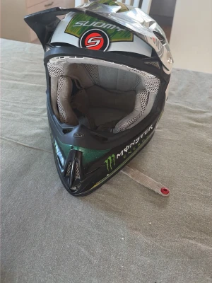Suomy crosshjälm Monster Energy - Säljer en Suomy crosshjälm med Monster Energy-design. Hjälmen är svart, vit och grön med stora loggor och detaljer. Den har ventilerande meshfoder och hakskydd. Den är inte ny så det är inte den bästa hjälmen men den funkar bra. Storlek finns på en bild