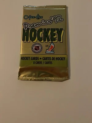 O-Pee-Chee Premier '92 Hockeykort - Säljer ett oöppnat paket O-Pee-Chee Premier '92 hockeykort. Förpackningen är guld- och grönfärgad och innehåller 8 samlarkort med NHL-tema. Perfekt för dig som gillar hockey och samlarkort.