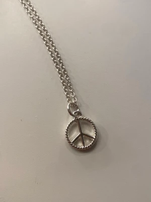 Silverfärgat halsband med peace-märke - Snyggt halsband i silverfärg med ett runt peace-symbol-hänge. Kedjan är tunn och har ett klassiskt karbinlås. Perfekt accessoar för dig som gillar stilrena smycken med en touch av retro. Helt oanvänd, ej äkta silver ❤️