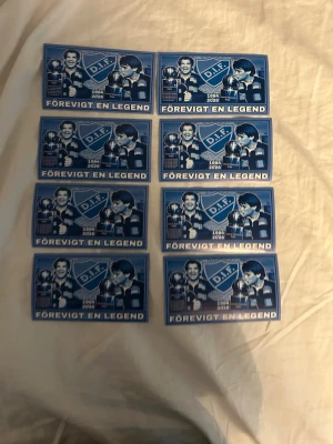 DIF klistermärken 'Förevigt en legend' - Säljer åtta blåa klistermärken med texten 'Förevigt en legend' och DIF-logga. Motivet visar en fotbollsspelare och årtalen 1964-2024. Perfekt för dig som vill visa ditt stöd för Djurgårdens IF.