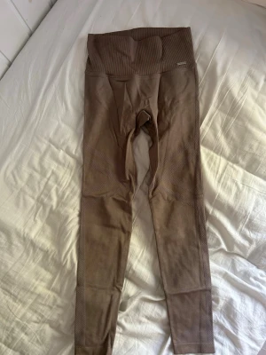 Beige seamless leggings Aim'n - Säljer ett par beige seamless leggings från Aim'n med hög midja och ribbad linning. Materialet är stretchigt och följsamt, perfekt för träning eller chill. Diskret Aim'n-logga framtill. Snygg passform och stilren design.