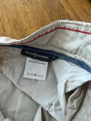 Beige bomullsshorts från Race Marine - Säljer ett par klassiska beige shorts från Race Marine i 100% bomull. De har en enkel design med fickor fram och diskret knappstängning. Perfekta för varma dagar och lätta att matcha med t-shirt eller skjorta.