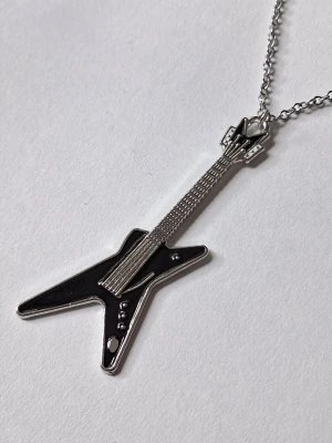 Halsband med gitarrhängsmycke - Coolt halsband med ett hängsmycke i form av en elgitarr. Smycket är i silverfärgad metall med svart detaljer och har en unik, kantig design som verkligen sticker ut. Perfekt för dig som gillar musik och vill ha något annorlunda runt halsen.