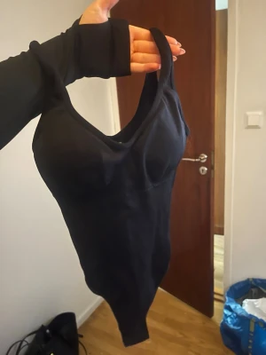 Svart body med smala axelband XS - Säljer en svart body med smala axelband och djup urringning. Tillverkad i stretchigt material med 92% polyamid och 8% elastan för en tight och bekväm passform. Perfekt att styla under skjortor eller tröjor för en clean look.