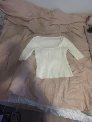 Vit ribbad topp  - Säljer en vit ribbad topp med snygg fyrkantig ringning och trekvartsärmar. Toppen är figurnära och har en stretchig känsla, perfekt att styla med jeans eller kjol. Materialet är mjukt och bekvämt.