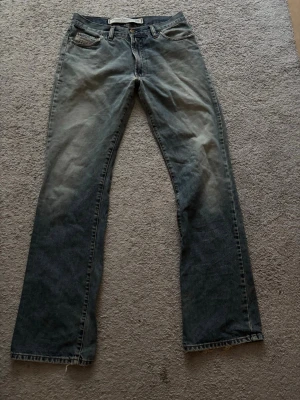 Blå raka jeans från Diesel - Säljer ett par klassiska blå jeans från Diesel med raka ben och femficksmodell. Jeansen har slitna detaljer och en tvättad look, samt Diesel-logga på myntfickan. Perfekta för en avslappnad stil.