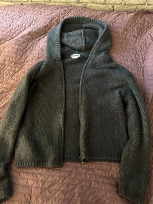 Grå stickad hoodie från Weekday - Mysig grå stickad hoodie från Weekday med dragkedja framtill och stor huva. Tröjan har en enkel, rak passform och är tillverkad i ett mjukt stickat material som passar perfekt för kyliga dagar.