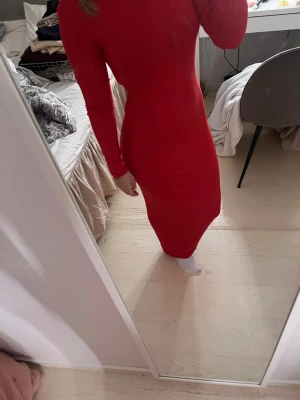 Röd långärmad klänning med öppen rygg - Snygg röd långklänning med lång ärm och en riktigt cool öppen rygg. Klänningen har en tight passform som framhäver figuren och är perfekt för dig som vill sticka ut. Enkel och stilren design utan mönster.