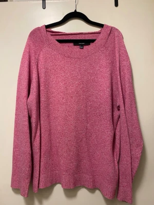 Rosa stickad tröja från VeroModa - Mysig rosa stickad tröja från VeroModa med bred ribbad halsringning och långa ärmar. Tröjan har en avslappnad passform och ribbade muddar vid ärmslut och nederkant. Perfekt för lager på lager och enkel att styla till jeans eller kjol. 