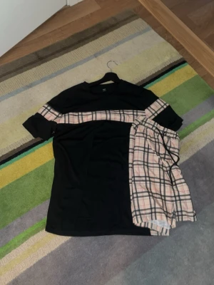 Svart pyjamas med rutiga detaljer - Snygg svart pyjamas med kortärmad t-shirt och matchande shorts. T-shirten har en bred beige-rosa rutig rand över bröstet och ärmarna. Kan gå ner i pris vid snabb affär 