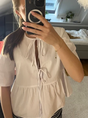 Vit blus med knyt och volang - Söt vit blus med två knytband framtill och lätt v-ringning. Blusen har korta ärmar och en volang nedtill💗använd en gång