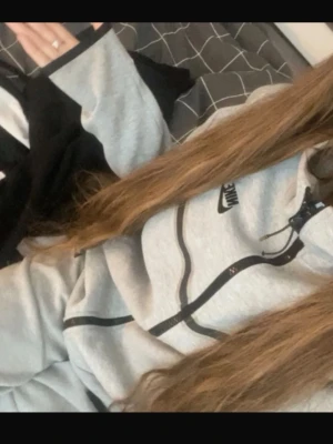 Grå Nike hoodie med svarta detaljer - Snygg grå hoodie från Nike med svarta dragkedjor och detaljer. Klassisk huva och Nike-logga på bröstet. Perfekt för en sportig och avslappnad stil. Tillverkad i mjukt material för extra komfort. Plus byxor!!