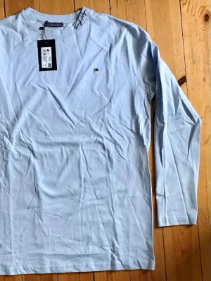 Ljusblå långärmad topp Tommy Hilfiger - Snygg ljusblå långärmad topp från Tommy Hilfiger med diskret logga på bröstet. Tillverkad i mjuk bomull som känns skön mot huden. Enkel och stilren design som passar till det mesta.