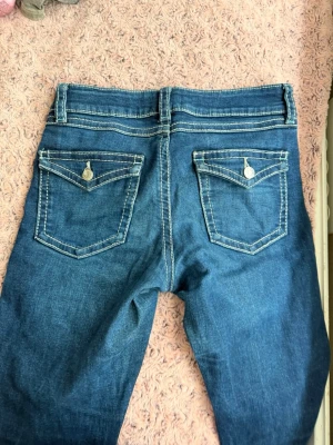 Blå jeans med kontrastsömmar - Snygga blå jeans med tydliga vita kontrastsömmar och klassiska fem fickor. Bakfickorna har lock och silverfärgade knappar. Jeansen har normal midja och bälteshällor. Perfekta för en avslappnad och trendig look.