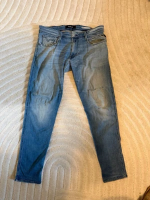 Ljusblå slim fit jeans från Replay - Snygga ljusblå slim fit jeans från Replay med klassisk femficksdesign och diskreta slitningar. Jeansen har en något tvättad look och detaljerade sömmar vid fickorna. Perfekta för en avslappnad och trendig stil.