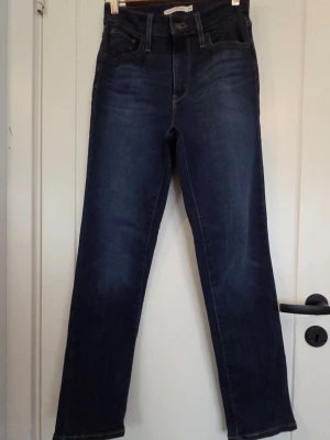 Mörkblå high rise straight jeans W26 L 30 - Snygga mörkblå jeans från Levi's med high rise och rak passform. Klassisk femficksmodell med knapp och dragkedja. Jeansen har subtila slitningar och är tillverkade i ett mjukt denimtyg som sitter bekvämt hela dagen.