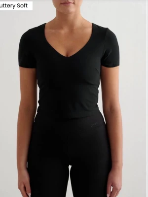 Bralette topp - En svart bralette topp med v-ringning och korta ärmar från aimn. Toppens material känns mjukt och har en inbyggd sport bh. Perfekt vid träning. Använd endast en gång. Priset på aim’ns hemsida är på 599 kr