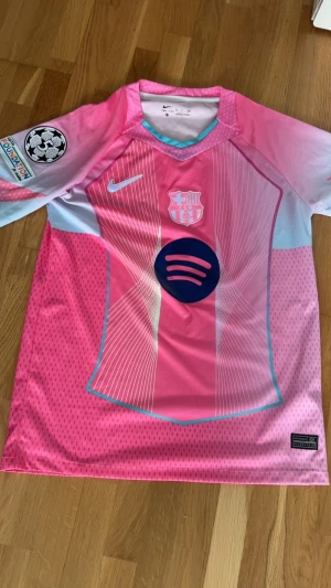 Barça Nike Dri-Fit rosa matchtröja - Säljer en FC Barcelona matchtröja från Nike i rosa och ljusblått med Dri-Fit-material. Tröjan har klubbmärke, Nike-logga, Champions League-märke på ärmen och Spotify-logga på bröstet. Perfekt för fotbollsträning eller att bära på läktaren.