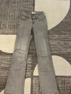 Grå bootcut jeans med brodyr - Säljer ett par grå bootcut jeans med snygga broderade detaljer på bakfickorna. Jeansen har klassisk femficksdesign och normalhög midja. Perfekta för dig som gillar en stilren look med lite edge.