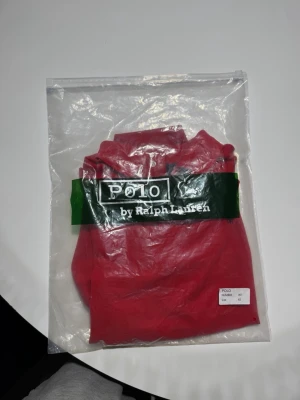 Röd pikétröja ralph lauren - Klassisk röd pikétröja från Polo Ralph Lauren med blå broderad logga på bröstet. Tröjan har krage, knappar framtill och är tillverkad i bomull. Perfekt för en stilren och sportig look. Storlek s-m mer mot m i mitt perspektiv 