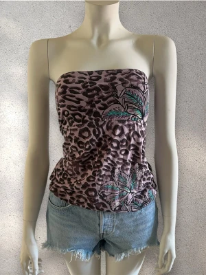 Leopardmönstrad topp med blommor - Topp från Brasilien  i ljuslila med leopardmönster och blommiga detaljer i grönt och svart. Toppen är axelbandslös och har en tight passform, perfekt för en trendig och cool look. Materialet känns mjukt och följsamt mot huden. #topp