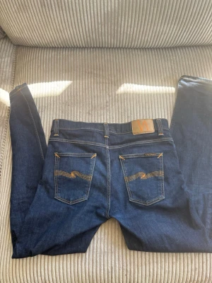 Jeans Nudie Jeans - Snygga mörkblå jeans från Nudie Jeans med klassisk femficksdesign och kontrastsömmar på bakfickorna. Jeansen har rak passform och är tillverkade i denim med läderpatch bak i midjan. Perfekta för en stilren och avslappnad look.