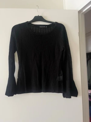 Svart stickad tröja  - Snygg svart stickad tröja  med lång ärm och rund halsringning. Tröjan har ett genombrutet mönster i zigzag och är tillverkad i ett tunt, mjukt material som ger en luftig känsla. Perfekt att styla lager på lager.